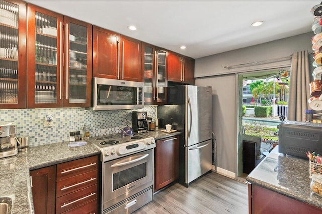 kitchen featuring light wood-type flooring, stainless steel appliances, tasteful backsplash, and dark stone countertops