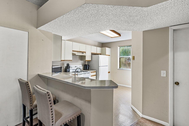 kitchen featuring a kitchen breakfast bar, kitchen peninsula, a textured ceiling, white appliances, and white cabinets