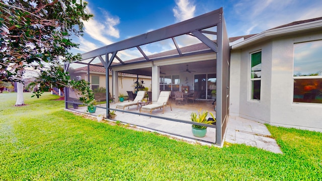 exterior space featuring a patio, a yard, ceiling fan, and glass enclosure