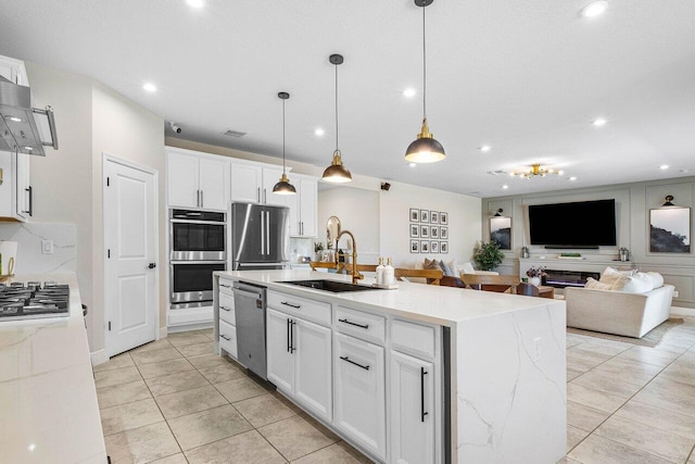 kitchen with white cabinetry, sink, stainless steel appliances, decorative light fixtures, and a kitchen island with sink