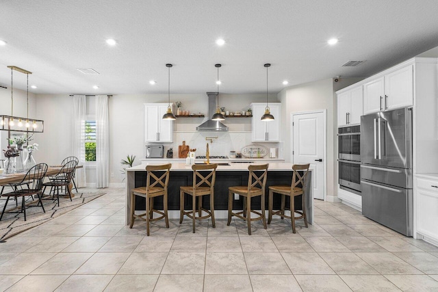 kitchen featuring a kitchen island with sink, wall chimney range hood, and appliances with stainless steel finishes