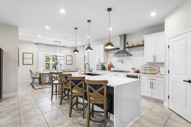 kitchen with light stone countertops, extractor fan, a kitchen island with sink, pendant lighting, and white cabinets