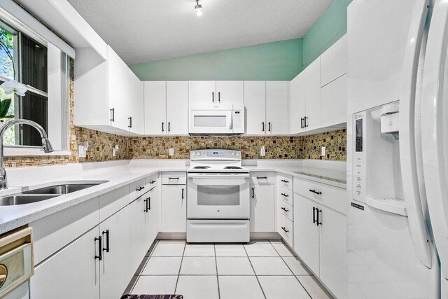 kitchen featuring white appliances, sink, vaulted ceiling, plenty of natural light, and white cabinetry