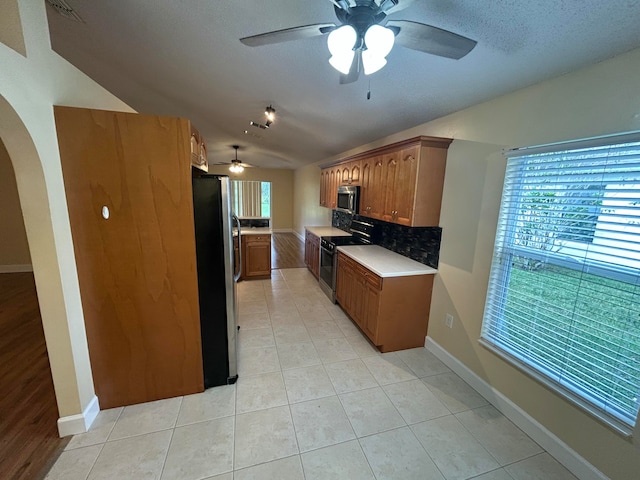 kitchen featuring tasteful backsplash, vaulted ceiling, a textured ceiling, light tile patterned flooring, and appliances with stainless steel finishes