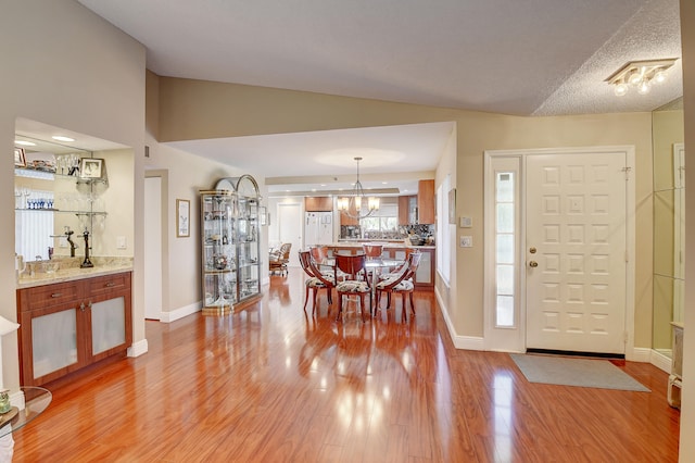 foyer with lofted ceiling, an inviting chandelier, a textured ceiling, and light wood-type flooring