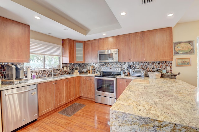 kitchen featuring decorative backsplash, light stone countertops, light wood-type flooring, stainless steel appliances, and sink