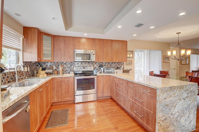 kitchen with sink, stainless steel appliances, light stone counters, decorative backsplash, and light wood-type flooring