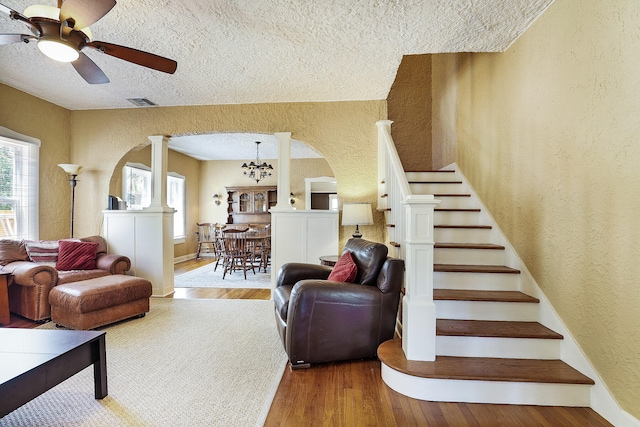 living room with a textured ceiling, ornate columns, ceiling fan with notable chandelier, and hardwood / wood-style flooring