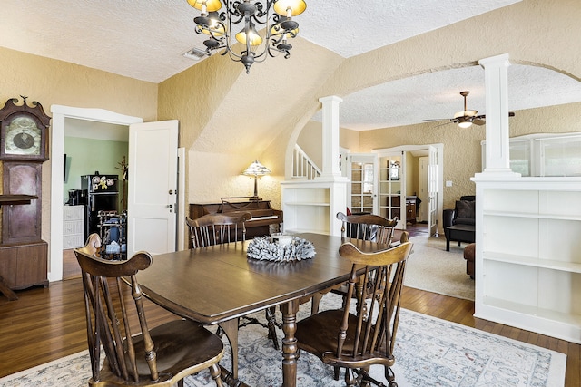 dining room with ceiling fan with notable chandelier, vaulted ceiling, dark hardwood / wood-style floors, ornate columns, and a textured ceiling