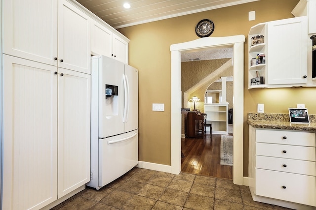 kitchen featuring white cabinets, dark stone countertops, white fridge with ice dispenser, ornamental molding, and dark hardwood / wood-style flooring