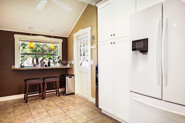 kitchen featuring white refrigerator with ice dispenser, stone counters, hanging light fixtures, vaulted ceiling, and white cabinetry