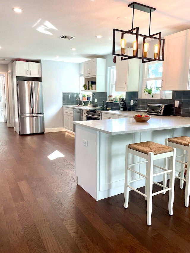 kitchen featuring white cabinets, appliances with stainless steel finishes, hanging light fixtures, and dark wood-type flooring