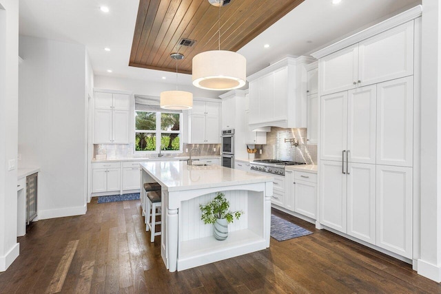 kitchen with a kitchen island with sink, white cabinetry, dark hardwood / wood-style flooring, and pendant lighting