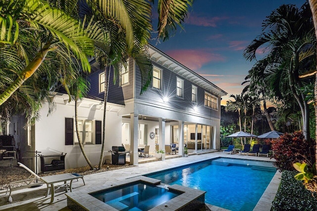 pool at dusk with area for grilling, a patio area, and an in ground hot tub