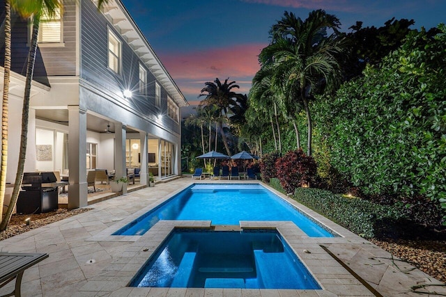 pool at dusk featuring an in ground hot tub and a patio