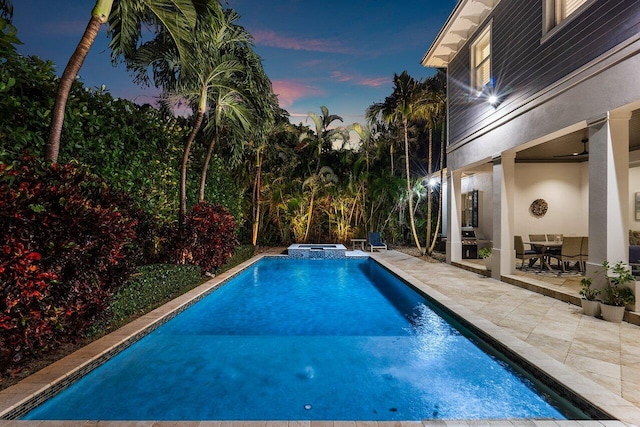 pool at dusk with a patio area and an in ground hot tub