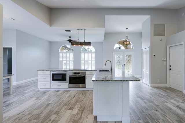 kitchen with pendant lighting, white cabinets, sink, stainless steel oven, and built in microwave