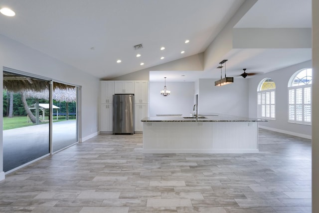 kitchen featuring pendant lighting, stone counters, white cabinetry, an island with sink, and stainless steel refrigerator