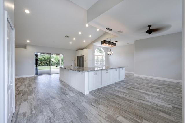 kitchen featuring white cabinetry, hanging light fixtures, stainless steel refrigerator, light hardwood / wood-style flooring, and a large island with sink