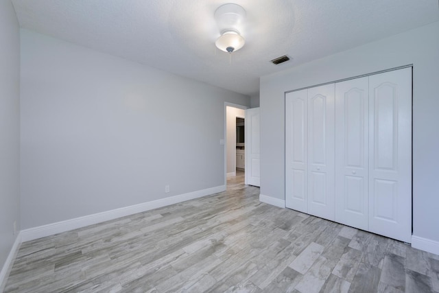 unfurnished bedroom with light hardwood / wood-style floors, a textured ceiling, and a closet