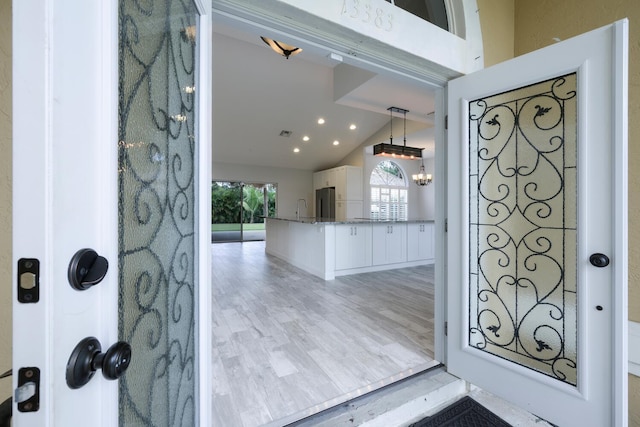 foyer entrance with sink, light hardwood / wood-style floors, a notable chandelier, and lofted ceiling