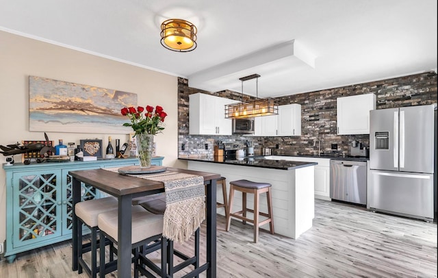 kitchen featuring appliances with stainless steel finishes, light wood-type flooring, backsplash, pendant lighting, and white cabinetry