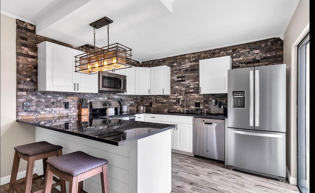 kitchen with kitchen peninsula, stainless steel appliances, white cabinetry, hanging light fixtures, and a breakfast bar area