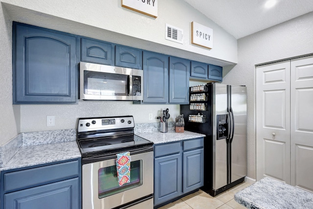 kitchen featuring appliances with stainless steel finishes, light tile patterned floors, blue cabinets, and vaulted ceiling