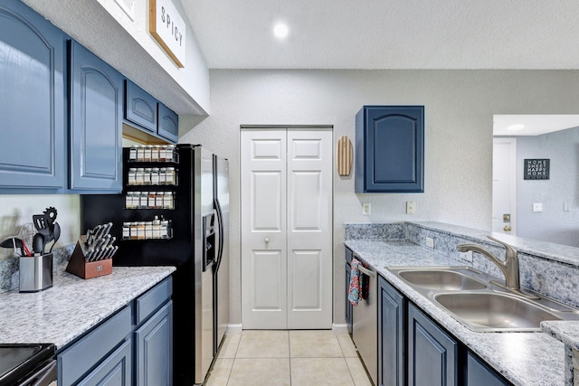 kitchen featuring a textured ceiling, stainless steel appliances, blue cabinets, sink, and light tile patterned floors