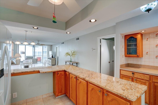 kitchen featuring light stone countertops, backsplash, kitchen peninsula, pendant lighting, and light tile patterned flooring