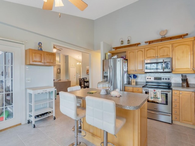 kitchen featuring light tile patterned floors, a kitchen breakfast bar, tasteful backsplash, a kitchen island, and appliances with stainless steel finishes