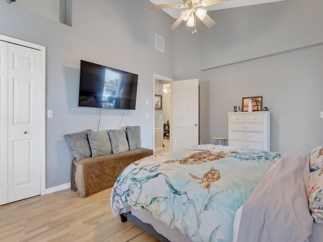 bedroom featuring ceiling fan, a closet, a towering ceiling, and light hardwood / wood-style floors