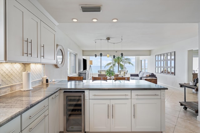 kitchen with tasteful backsplash, beverage cooler, hanging light fixtures, and white cabinets