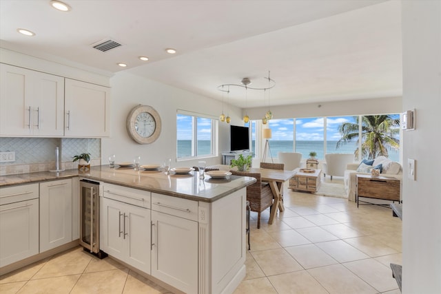 kitchen with white cabinetry, tasteful backsplash, hanging light fixtures, kitchen peninsula, and beverage cooler