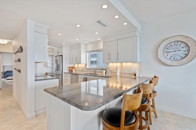 kitchen featuring sink, a breakfast bar area, appliances with stainless steel finishes, white cabinetry, and decorative backsplash