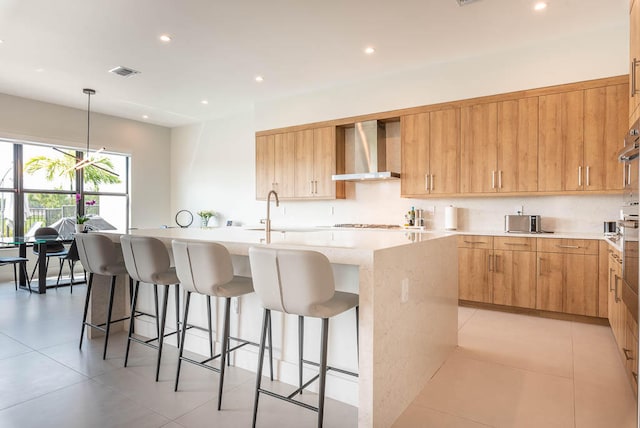 kitchen with decorative light fixtures, sink, a center island with sink, and wall chimney range hood