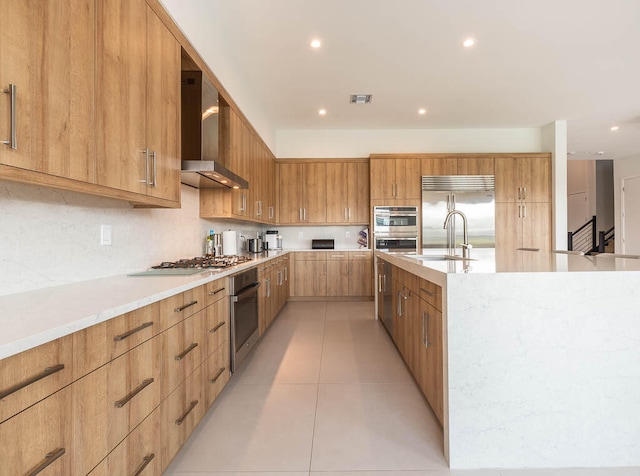 kitchen featuring wall chimney range hood, sink, decorative backsplash, light tile patterned floors, and appliances with stainless steel finishes