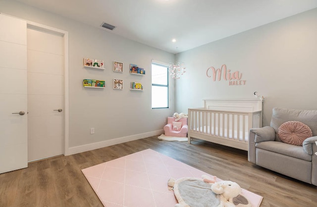 bedroom featuring wood-type flooring and a nursery area