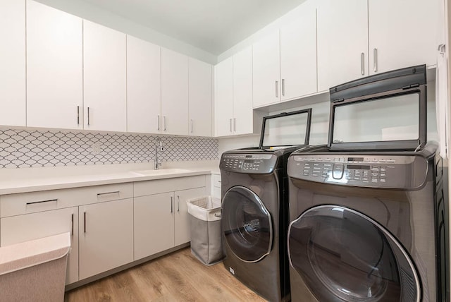 clothes washing area featuring separate washer and dryer, light hardwood / wood-style floors, cabinets, and sink