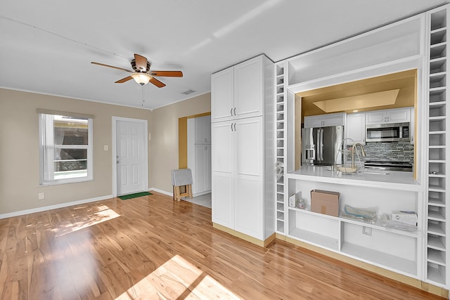 interior space with ceiling fan, light hardwood / wood-style flooring, backsplash, white cabinets, and appliances with stainless steel finishes