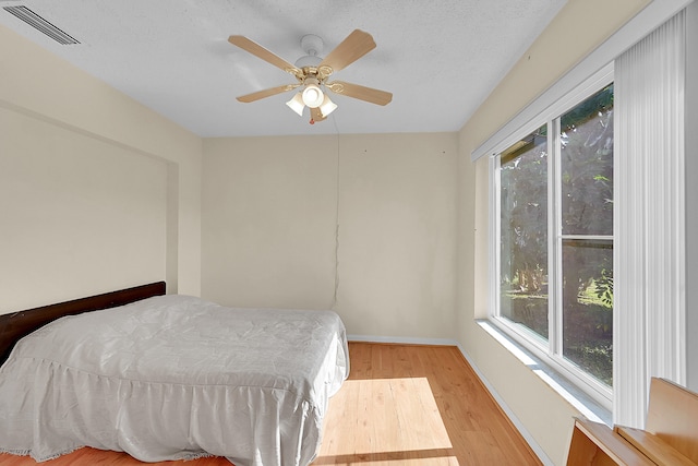 bedroom featuring multiple windows, ceiling fan, light hardwood / wood-style flooring, and a textured ceiling