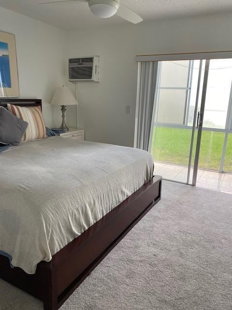 carpeted bedroom with a wall mounted AC, ceiling fan, a textured ceiling, and access to exterior