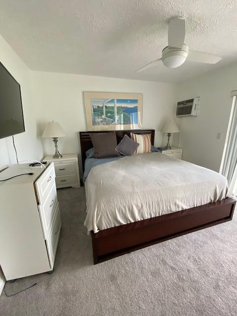 carpeted bedroom with a textured ceiling, an AC wall unit, and ceiling fan