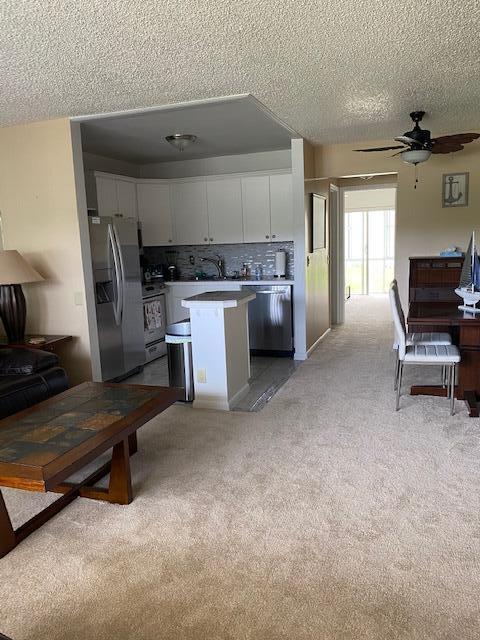 kitchen with tasteful backsplash, stainless steel appliances, light colored carpet, a center island, and white cabinetry