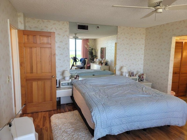 bedroom featuring a ceiling fan, wood finished floors, visible vents, wallpapered walls, and a textured ceiling