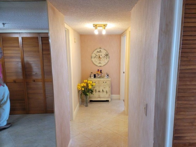 hall featuring tile patterned flooring, a textured ceiling, and baseboards