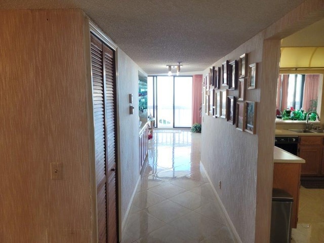 corridor with a sink, a textured ceiling, floor to ceiling windows, light tile patterned flooring, and baseboards