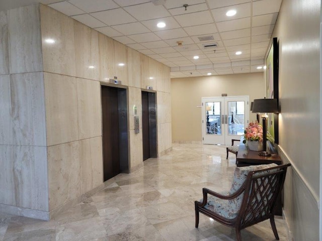 hallway with elevator, a drop ceiling, french doors, and a towering ceiling