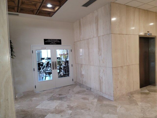 interior space featuring visible vents, coffered ceiling, a high ceiling, elevator, and french doors