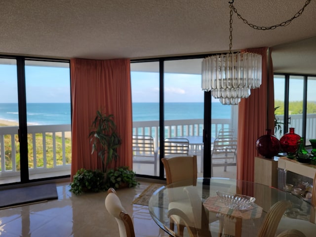 dining area featuring a view of the beach, a textured ceiling, a water view, and an inviting chandelier